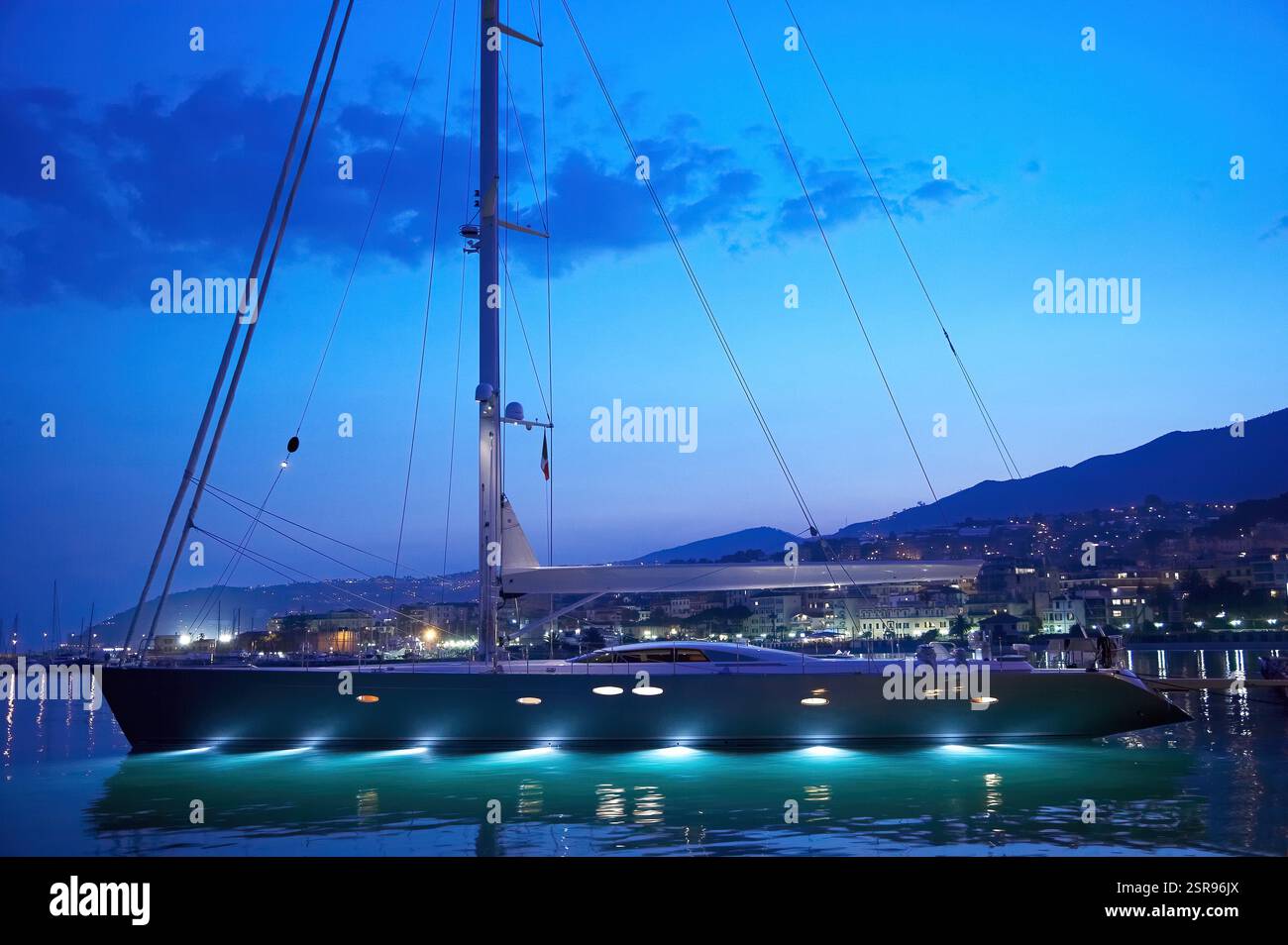 Yacht a vela di lusso Y2 con luci subacquee attraccate alla marina costiera illuminata durante il crepuscolo Foto Stock