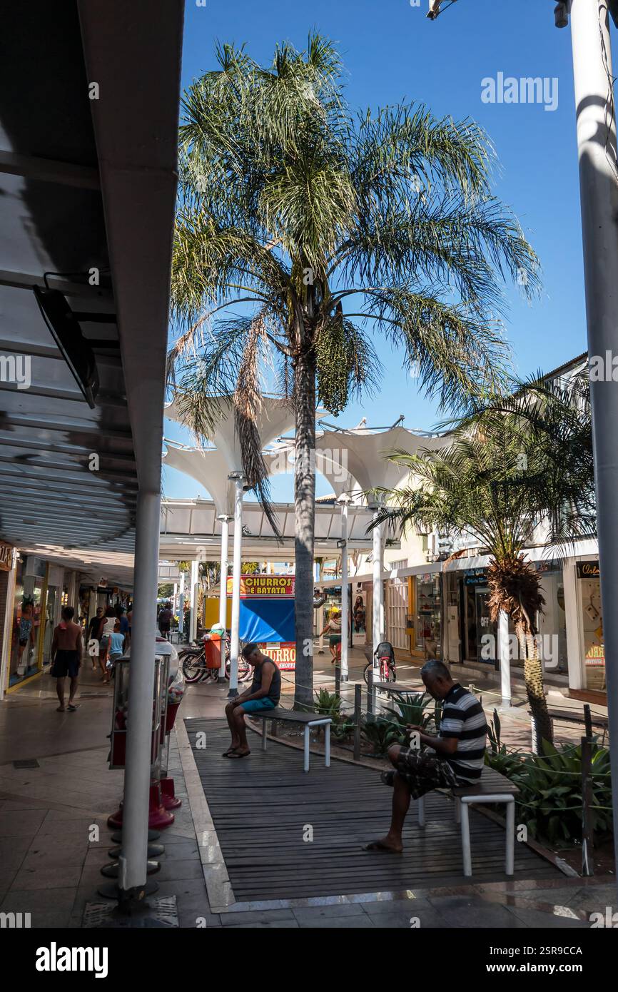 Corridoio commerciale ombreggiato all'interno del centro commerciale Rua dos Biquinis nel quartiere di Gamboa con boutique, bancarelle alimentari e aree di riposo nel tardo pomeriggio. Foto Stock