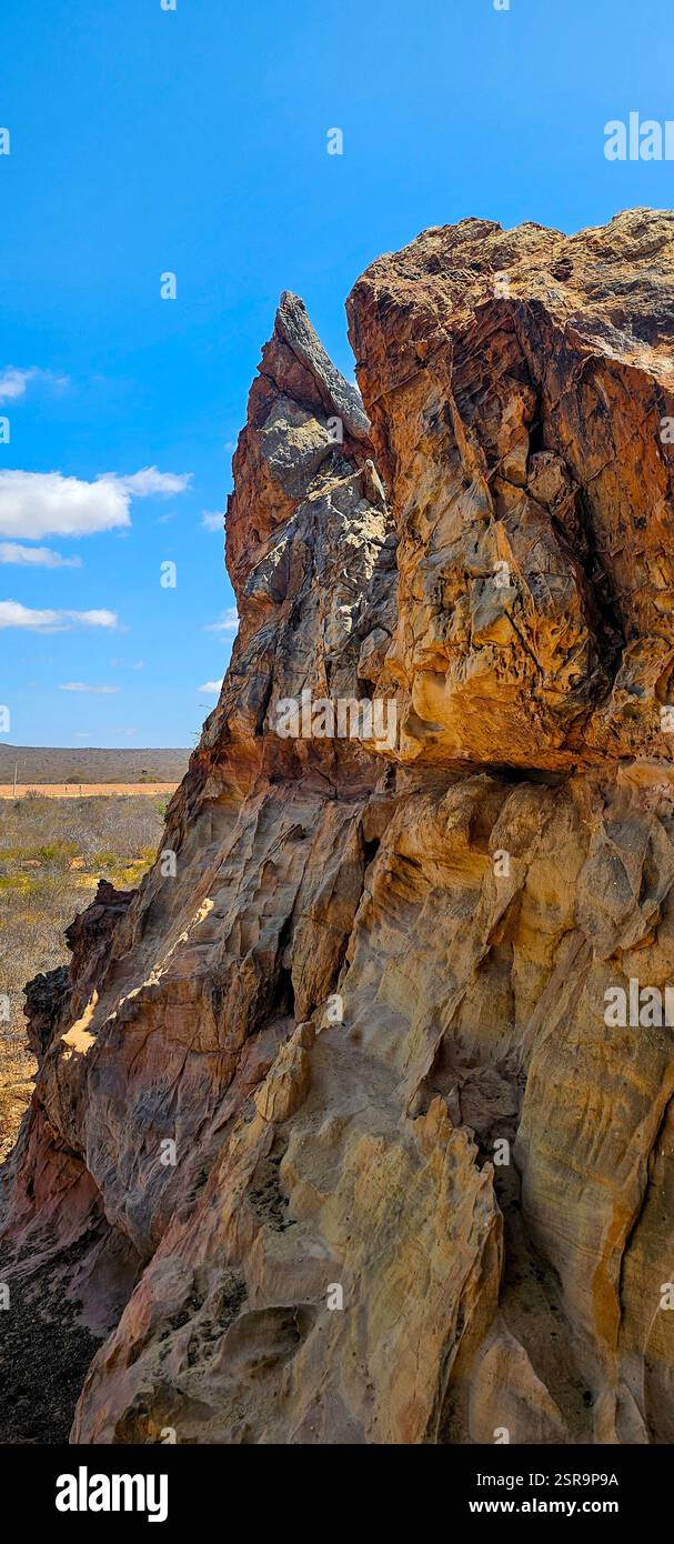 Formazione rocciosa torreggiante con consistenze ruvide sotto un cielo azzurro. La luce del sole mette in risalto i toni terrosi contro il vasto paesaggio, trasmettendo una S. - Immagine stock catturata con smartphone
