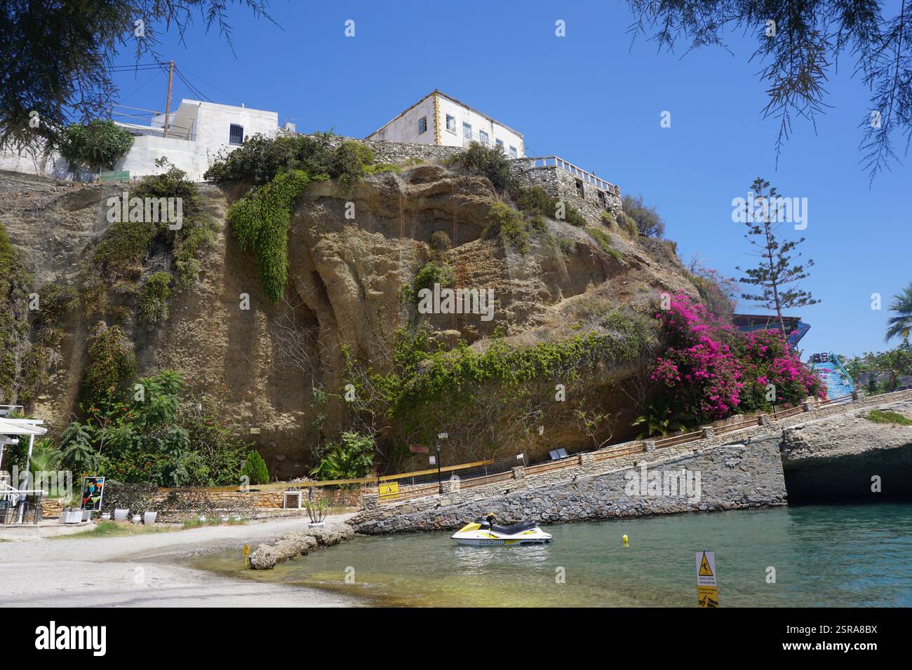 Vista del porto di Agia Galini, Grecia, con vista sulla scogliera che mostra aspre formazioni rocciose e una moto d'acqua sottostante Foto Stock