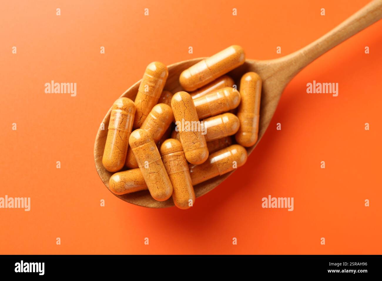 Capsule di curcuma in cucchiaio di legno su sfondo arancione, vista dall'alto Foto Stock
