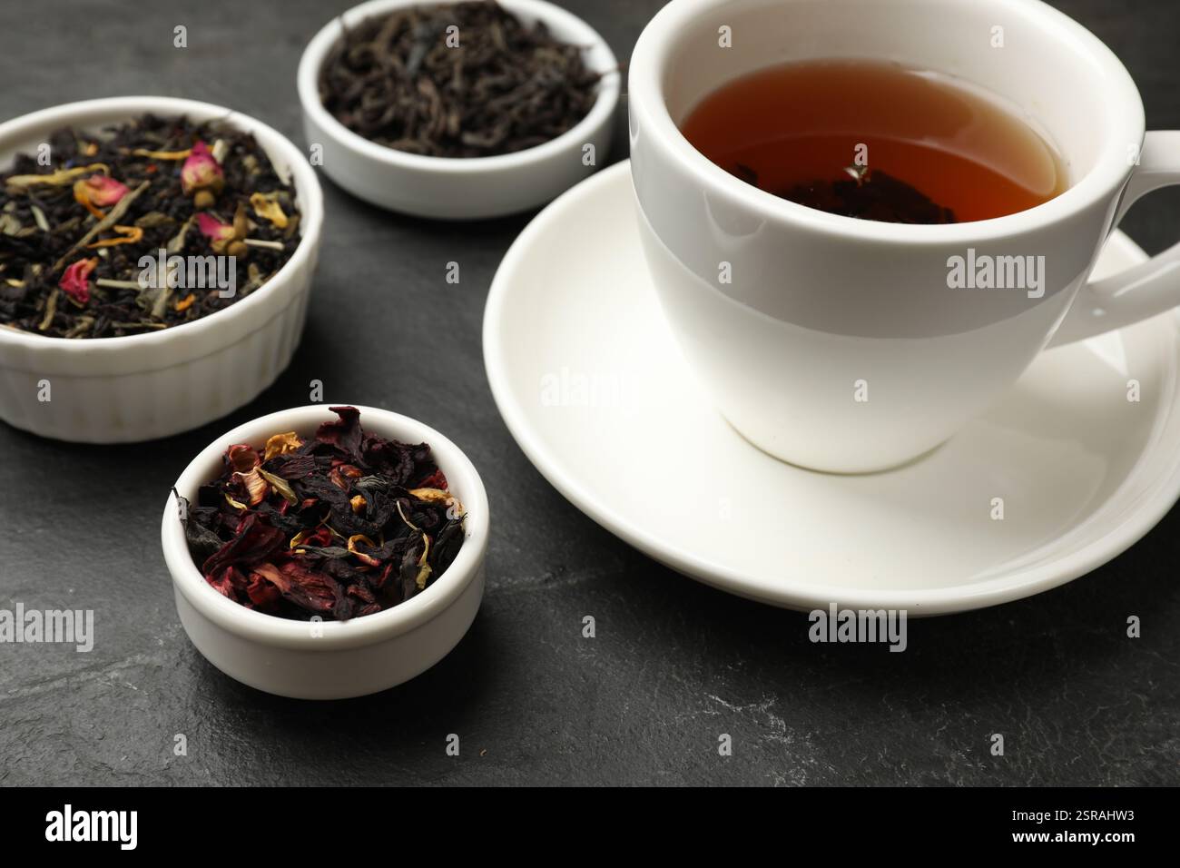 Tè aromatico e foglie secche sul tavolo nero, primo piano Foto Stock