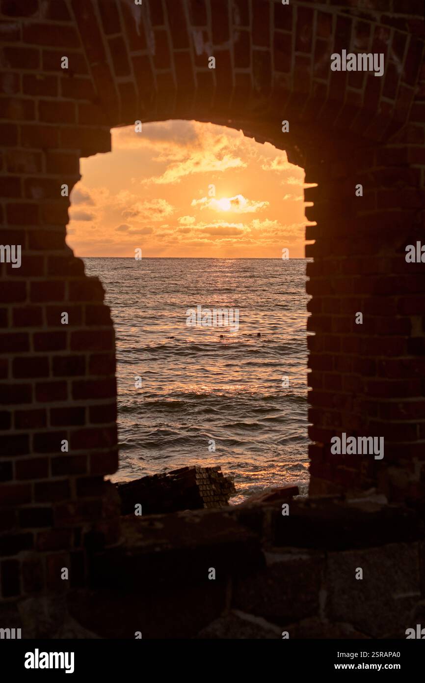 Accattivante tramonto sul mare incorniciato da finestre in mattoni, che evocano serenità e nostalgia con tonalità vibranti e onde dolci Foto Stock