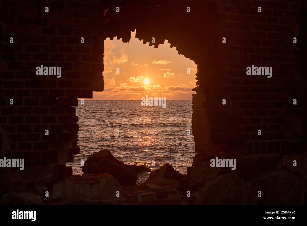 Accattivante tramonto sul mare incorniciato da finestre in mattoni, che evocano serenità e nostalgia con tonalità vibranti e onde dolci Foto Stock