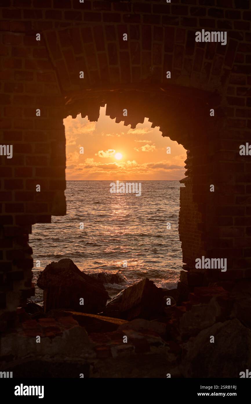 Accattivante tramonto sul mare incorniciato da finestre in mattoni, che evocano serenità e nostalgia con tonalità vibranti e onde dolci Foto Stock