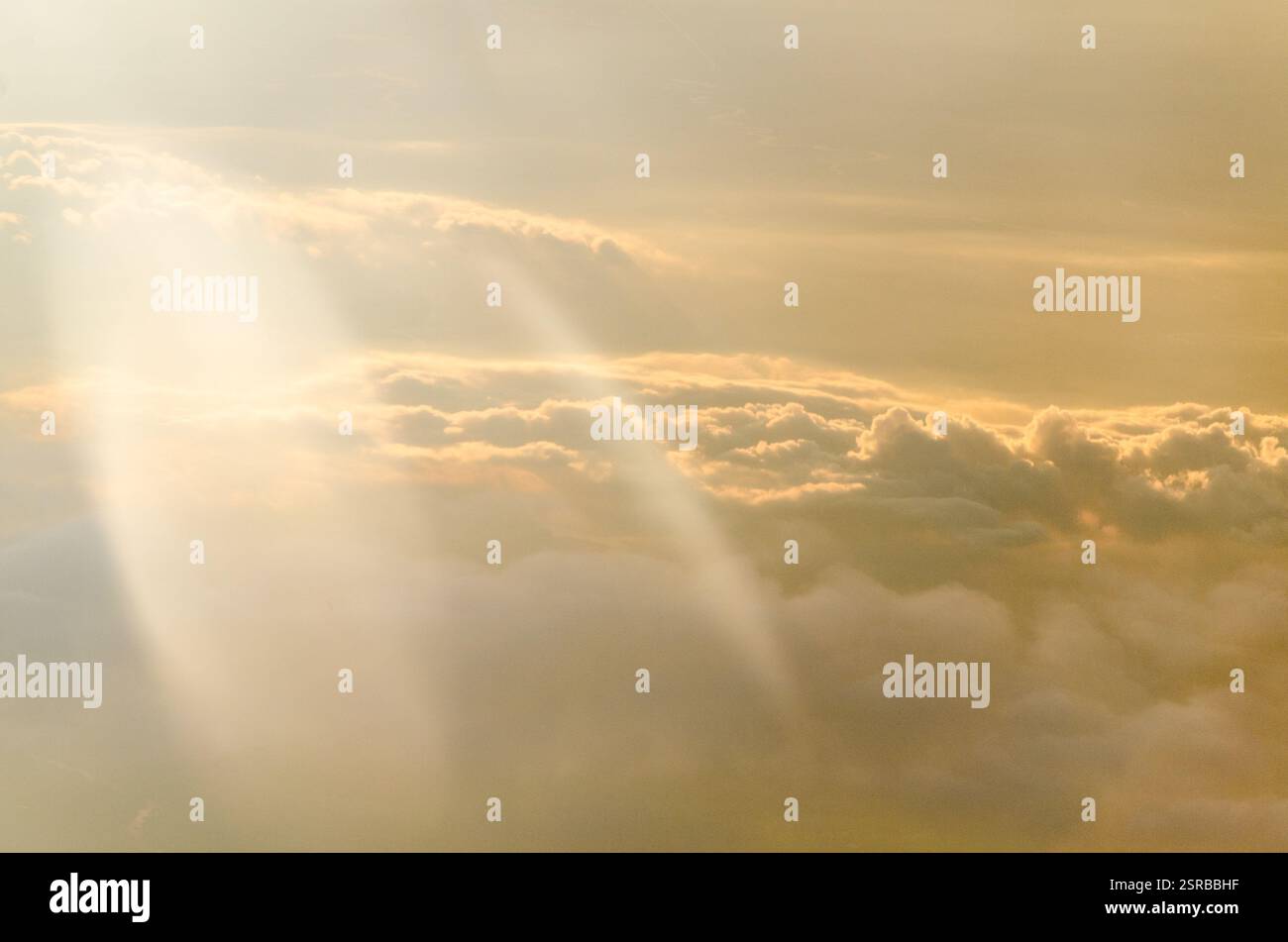 La luce soffusa del sole illumina le soffici nuvole, creando una tranquilla tonalità dorata. La vista aerea cattura la tranquilla atmosfera mattutina. I gradienti delicati evocano la calma A. Foto Stock