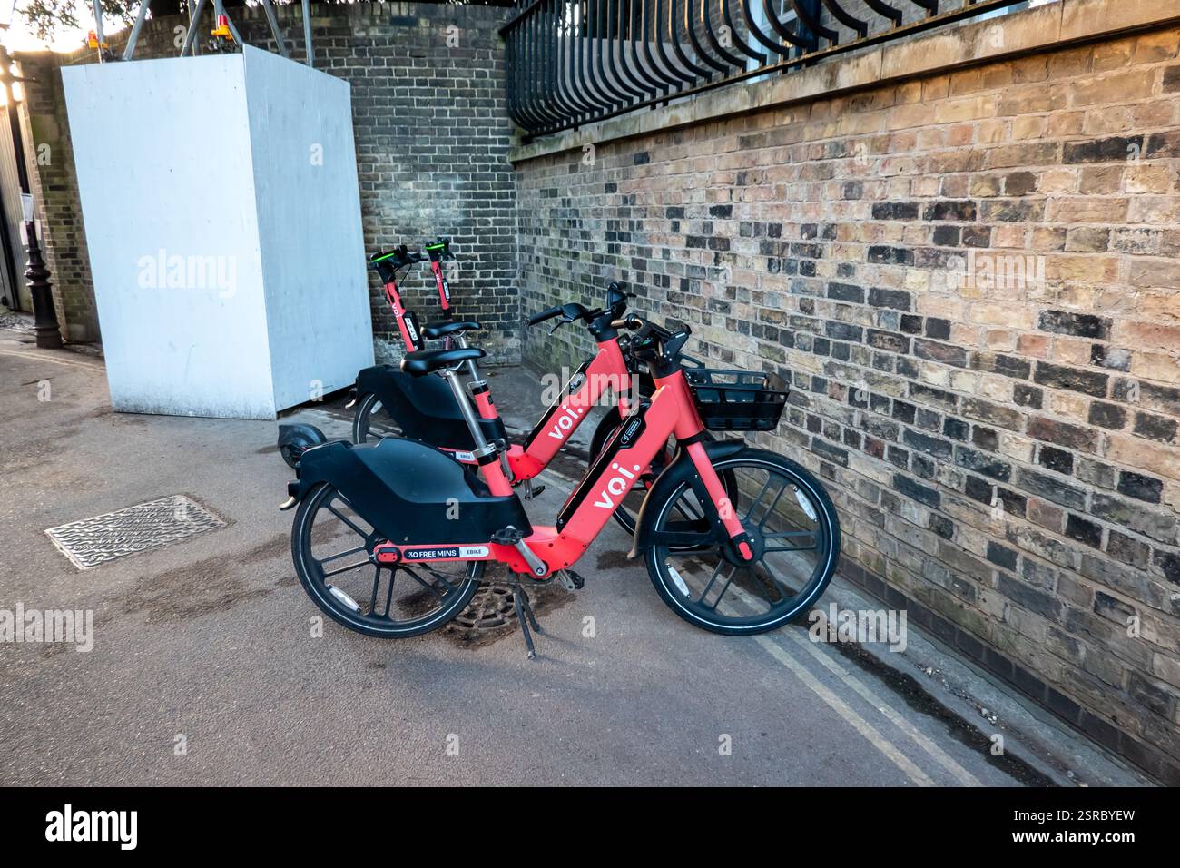 Due e-bike voi color corallo sono parcheggiate in una strada della città contro un muro di mattoni intempestivo, offrendo un'opzione di trasporto ecologica Foto Stock