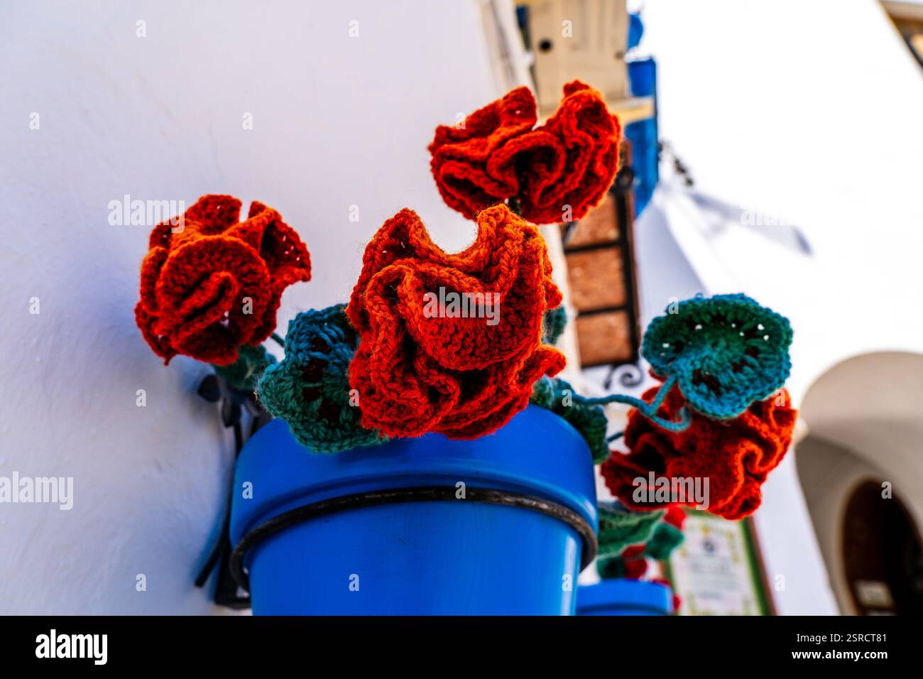 Rose all'uncinetto artigianali in pentole blu contro le pareti andaluse bianche di Iznajar Foto Stock