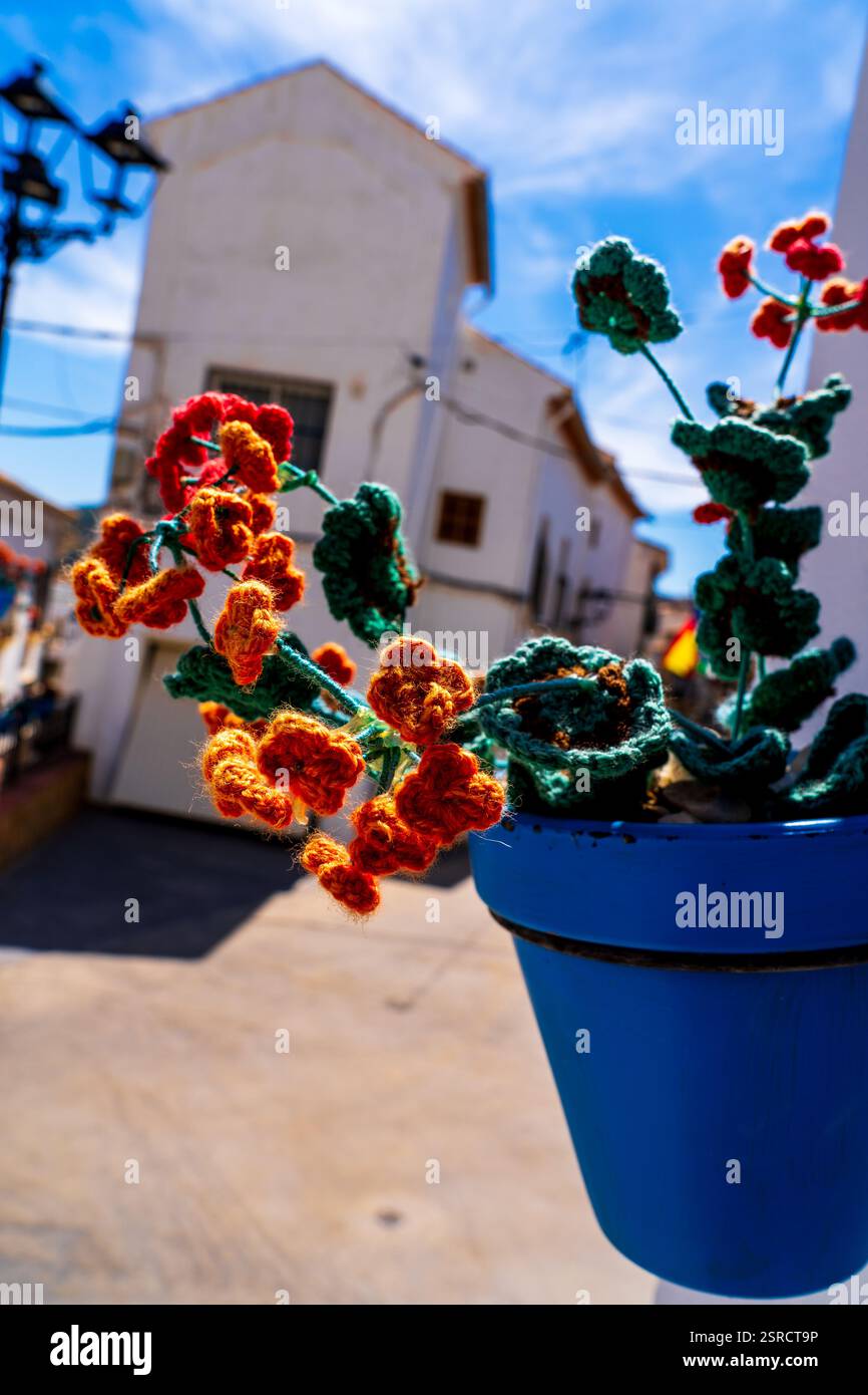I colorati fiori all'uncinetto in una pentola blu con un pittoresco sfondo del villaggio andaluso Foto Stock