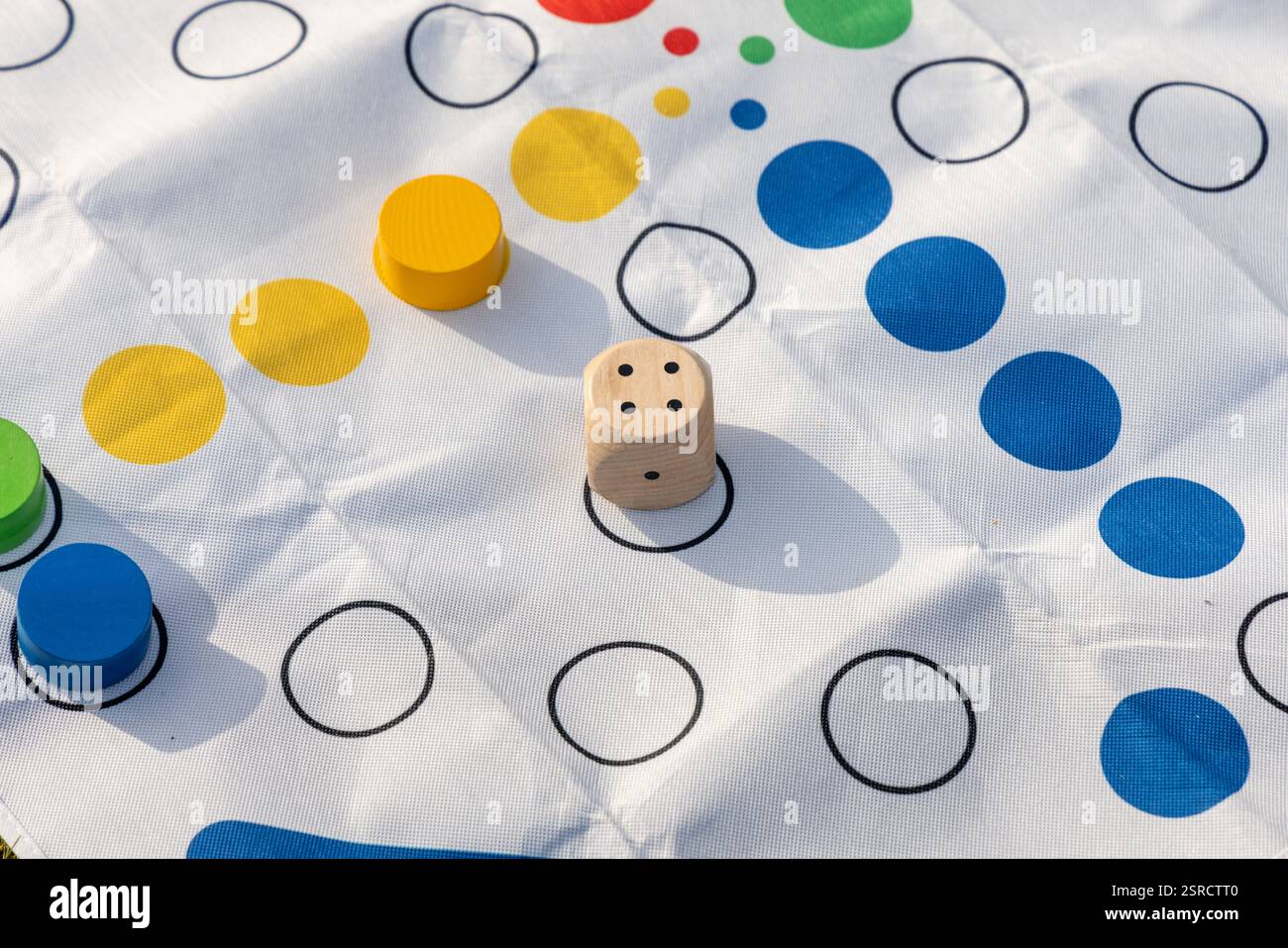 Un dado di legno poggia su un luminoso tappeto da gioco da tavolo con colorati spazi circolari e gettoni abbinati. Perfetto per illustrare il divertimento e il tempo libero Foto Stock