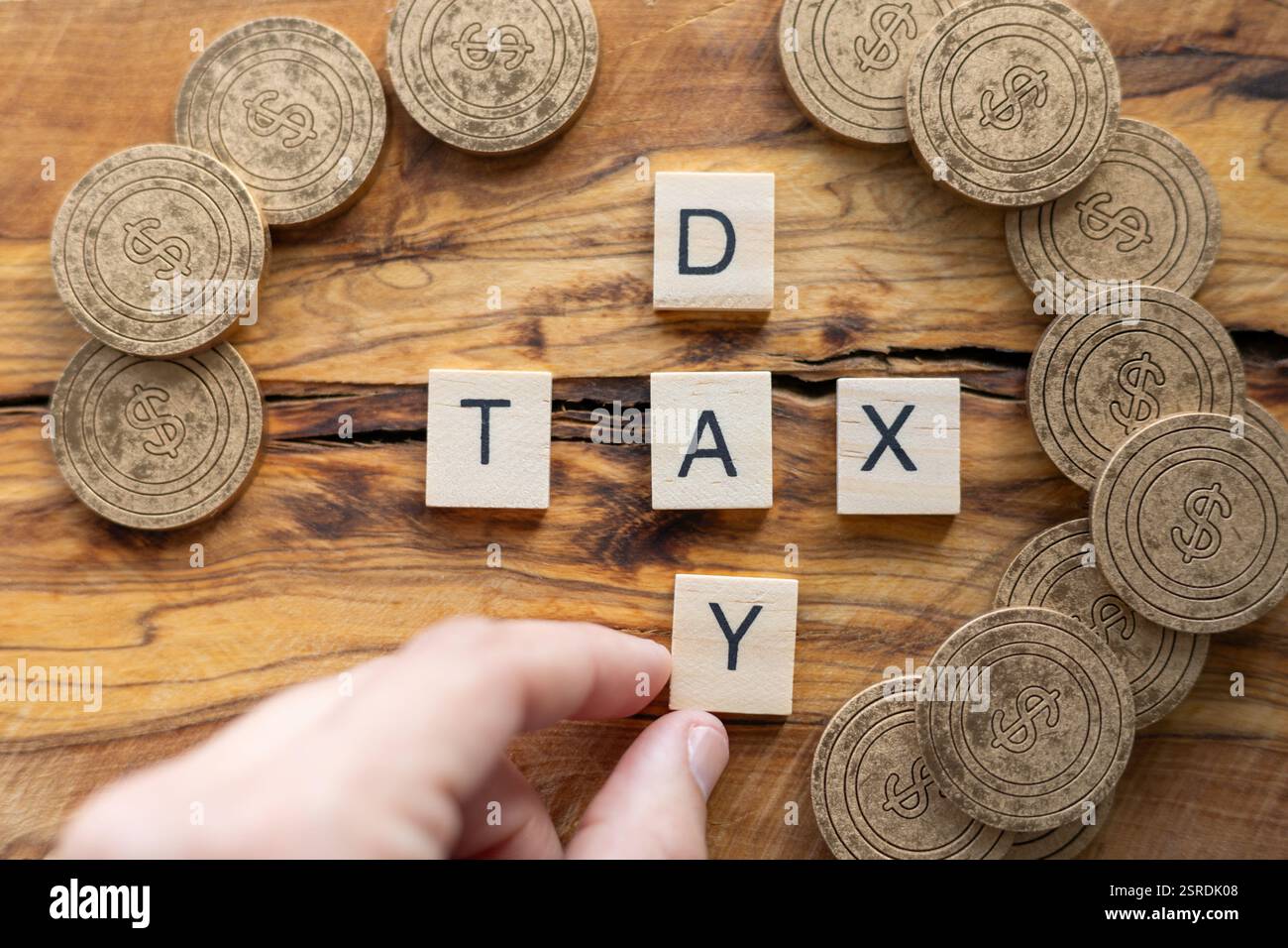 Mettere a mano lettere di legno per scrivere IL GIORNO DELLE TASSE su una superficie rustica di legno, circondata da monete di legno con segni di dollaro. Concetti fiscali, finanziari, economici Foto Stock