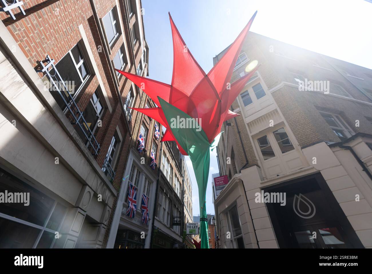 Grande struttura a forma di fiore rossa e verde su Carter Lane, con bandiere Union Jack sugli edifici. Probabilmente un'installazione artistica temporanea. Foto Stock