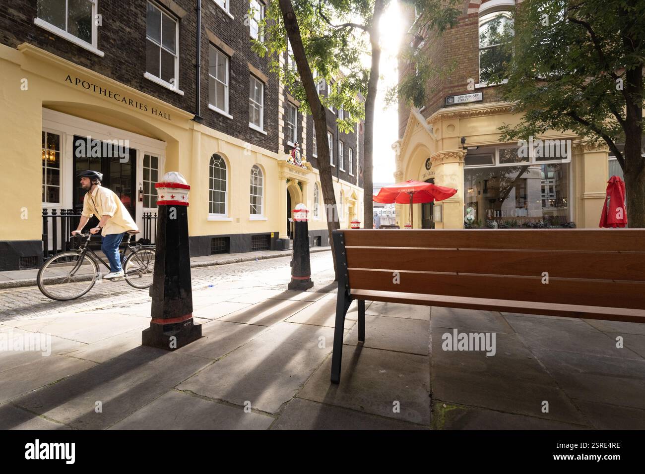 Il ciclista passa davanti all'Apothecaries Hall, a Londra, oltre il ristorante Gleam. La luce del sole proietta ombre. Black Friars Lane Foto Stock