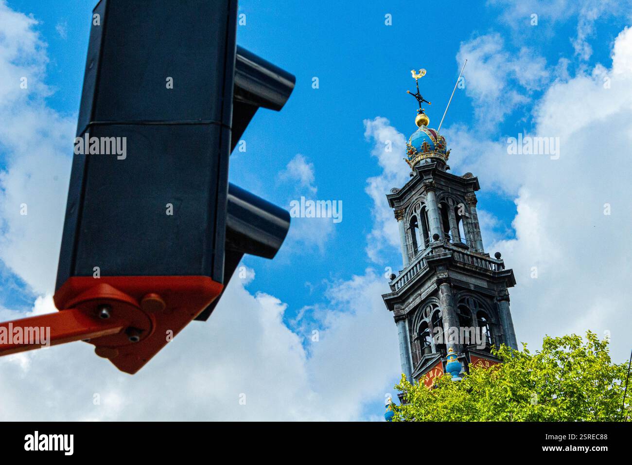 Torre della chiesa di Amsterdam incorniciata da un semaforo, che unisce contrasti storici e urbani. Cielo blu vibrante con tonalità di rosso e verde Foto Stock