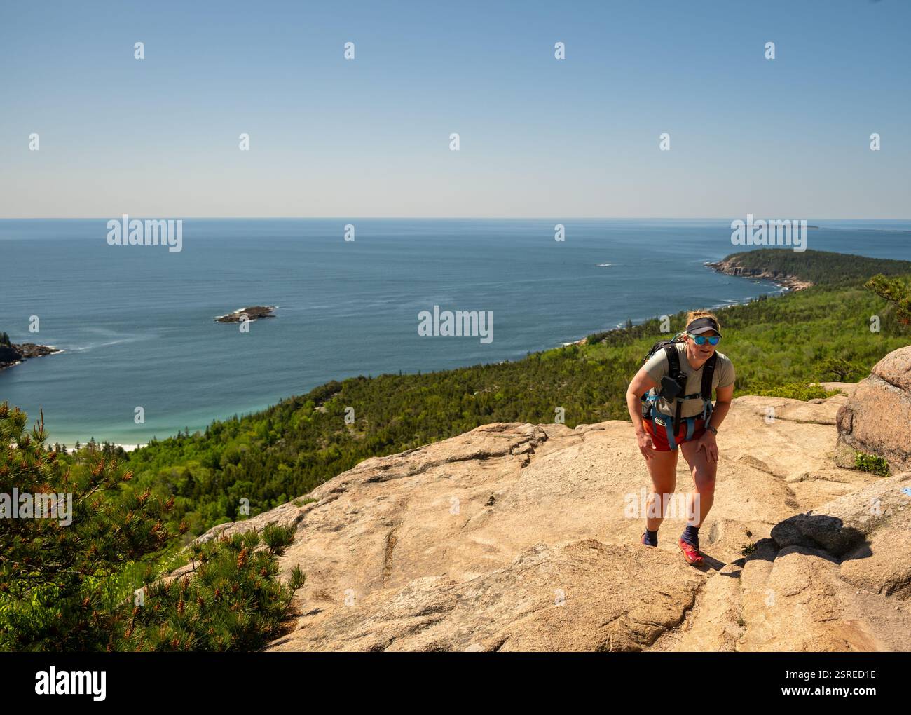Una donna fa un'escursione sulla ripida parete rocciosa del Beehive nel Parco Nazionale dell'Acadia Foto Stock