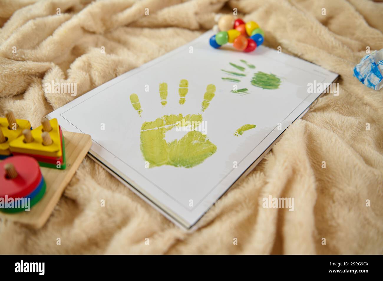 Colorate stampe a mano per bambini che adornano un foglio su un'accogliente coperta circondata da giocattoli che rappresentano la creatività, il gioco e i momenti di gioia. Foto Stock