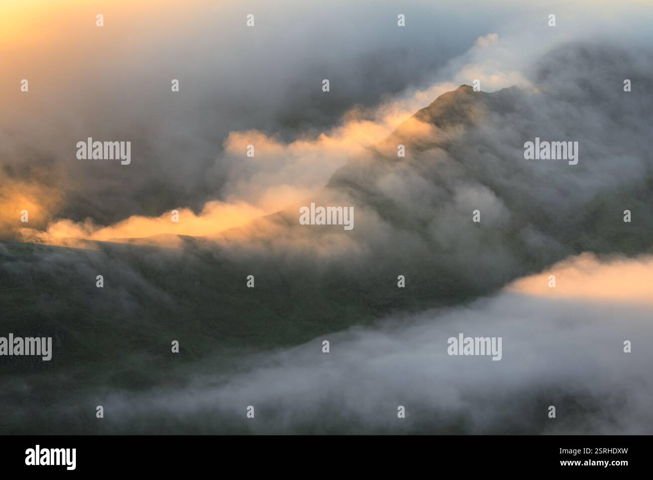Misty Lake District picchi montuosi con luce del sole dorata che illumina le nuvole. Fairfield Horseshoe, Regno Unito. Foto Stock