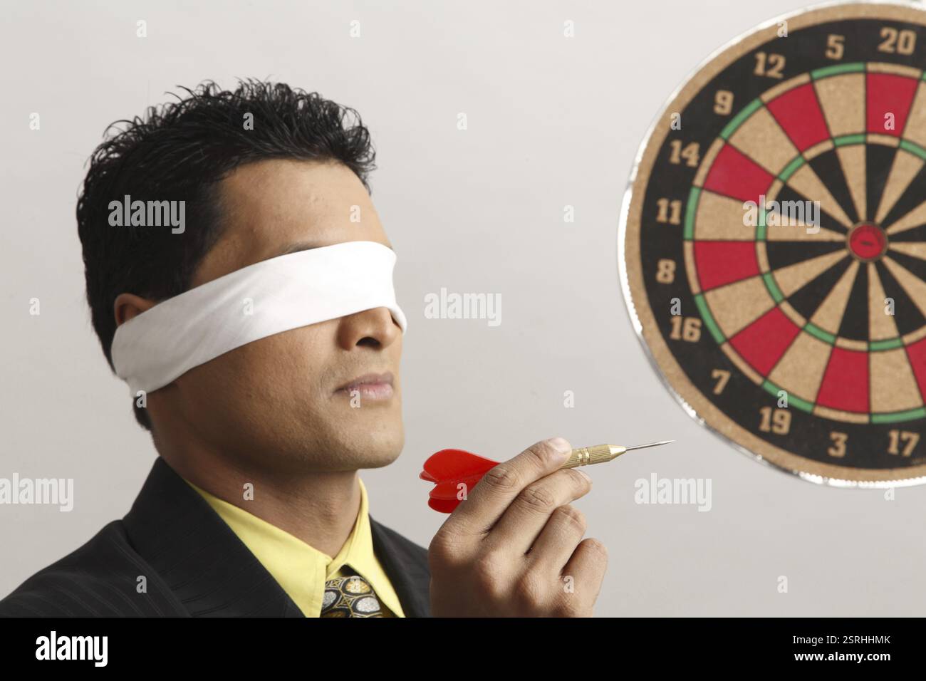 Imprenditore azienda DART in una mano e freccette sulla parete mirando a occhi chiusi signor#703T Foto Stock