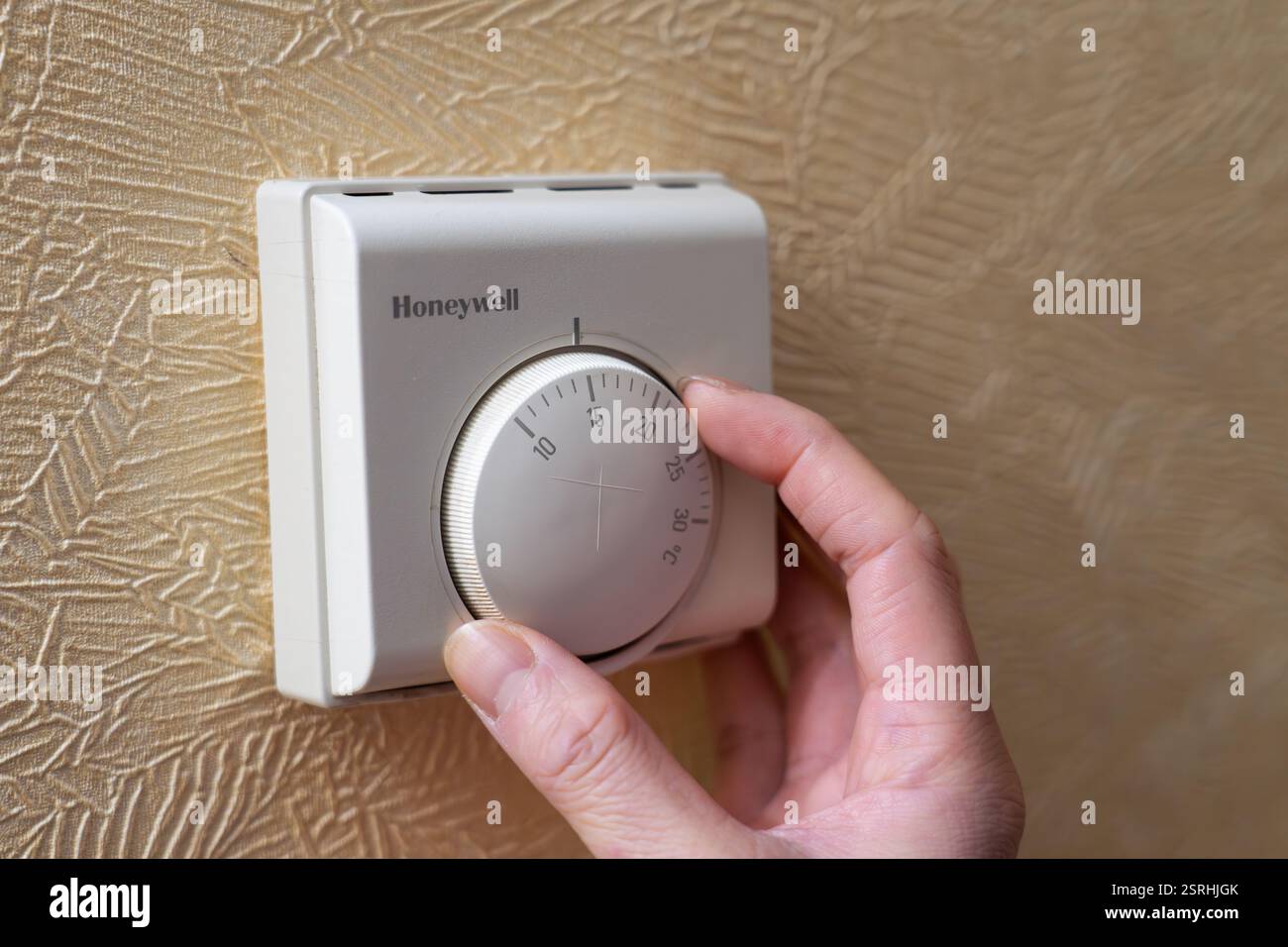 La mano di una donna che gira un termostato Honeywell in una casa, in Inghilterra. Concetto: Riscaldamento centralizzato, bollette energetiche, limite energetico, prezzo del gas Foto Stock
