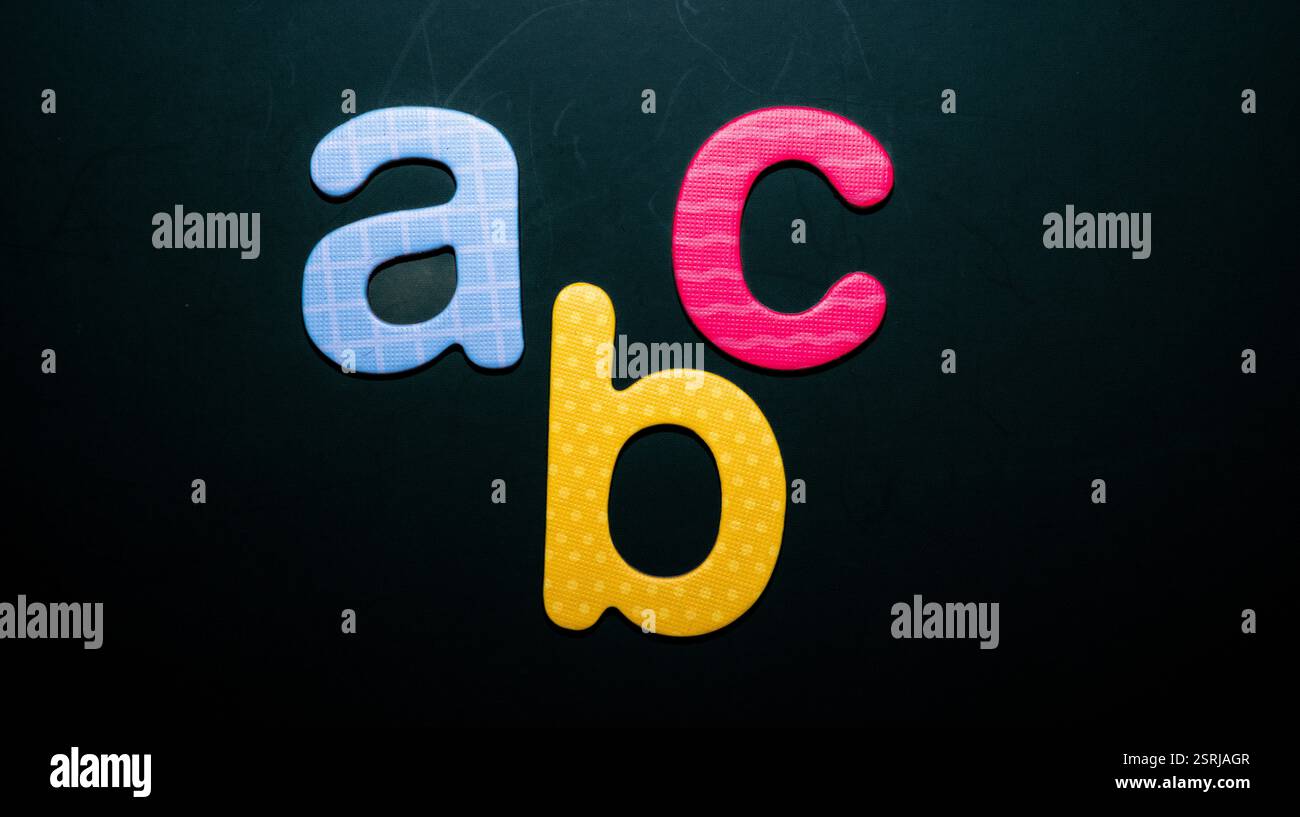 Tre lettere colorate in schiuma, "a", "b" e "c", disposte su uno sfondo scuro, simboleggiano l'educazione della prima infanzia e l'apprendimento dell'alfabeto Foto Stock
