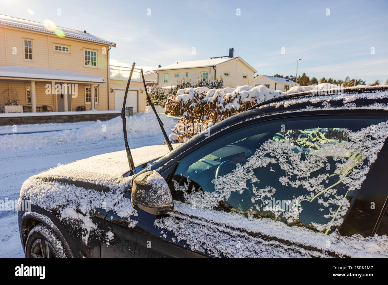 Auto nera ghiacciata con tergicristalli rialzati ricoperti di neve vicino a una casa residenziale nelle fredde giornate invernali. Svezia. Foto Stock