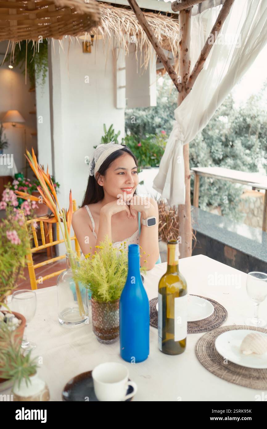 Bella donna asiatica che indossa il copricapo seduto e si rilassa sul tavolo da pranzo con bevande decorate nel caffè durante il fine settimana Foto Stock