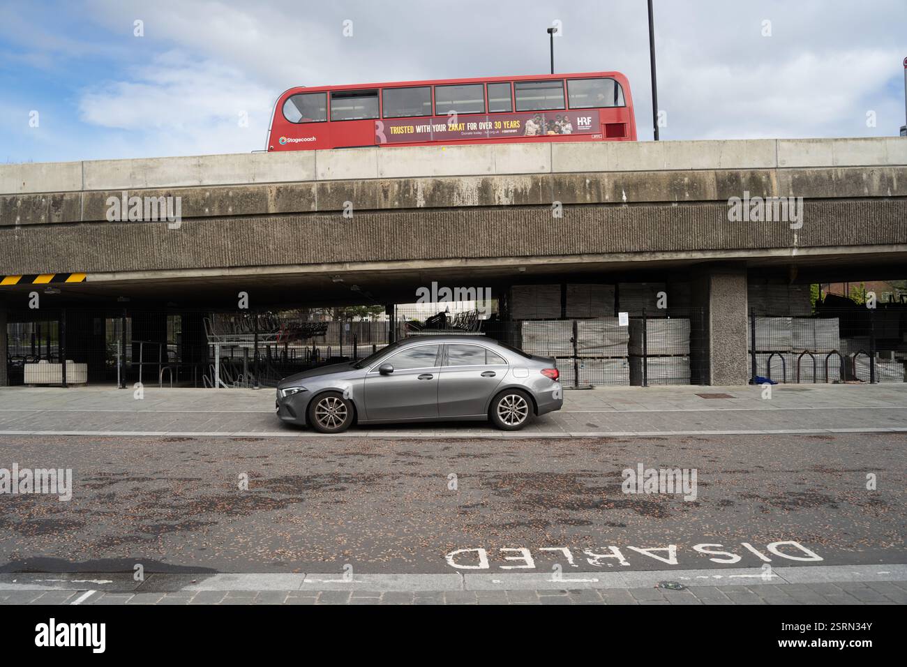 Mercedes grigia parcheggiata sotto un ponte in un parcheggio per disabili ad Abbey Woods Londra, Regno Unito. Un autobus rosso della Stagecoach passa sopra la testa. Foto Stock