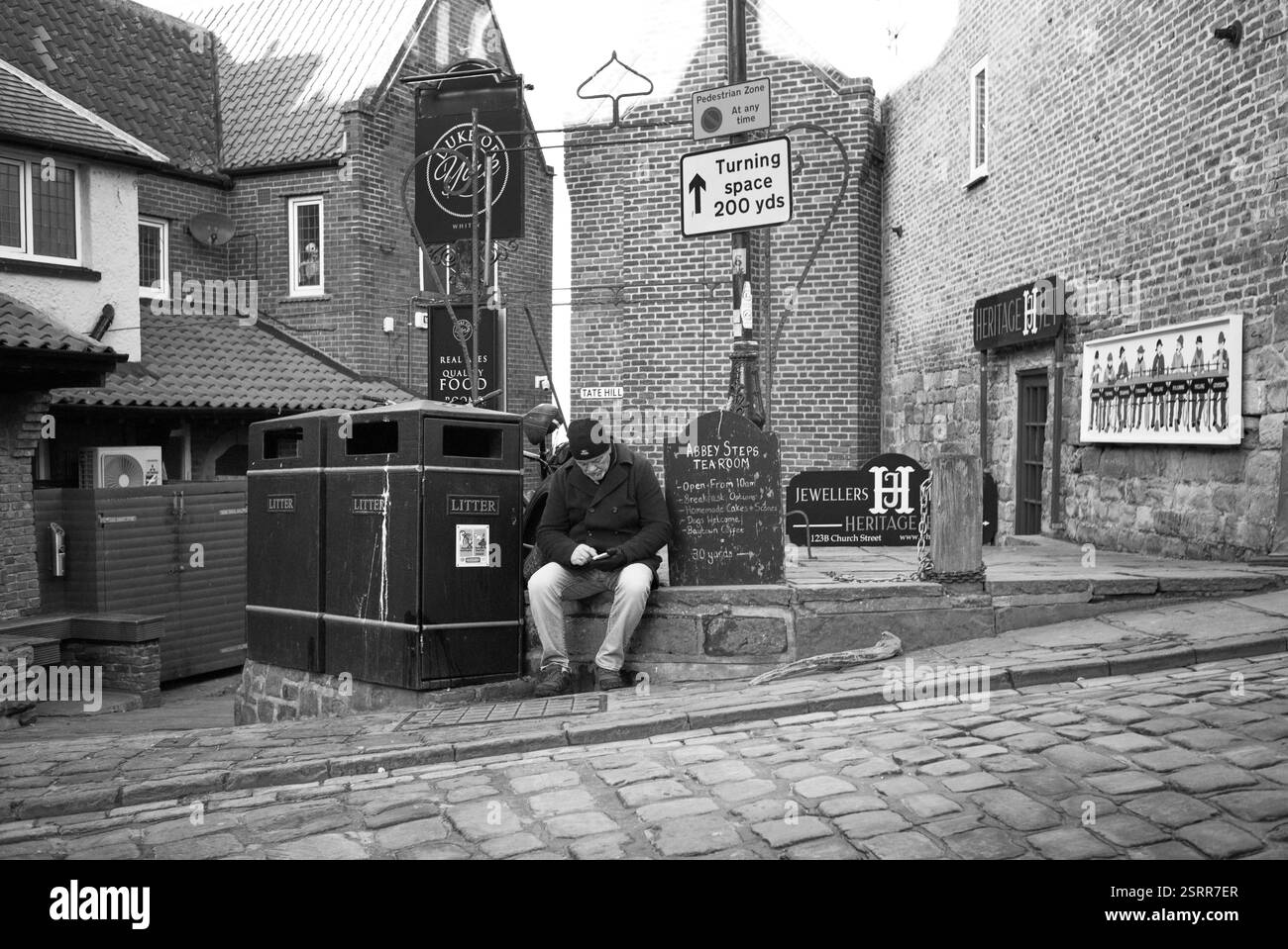 Un uomo anziano seduto a guardare un telefono nella zona di Tate Hill a Whitby Foto Stock