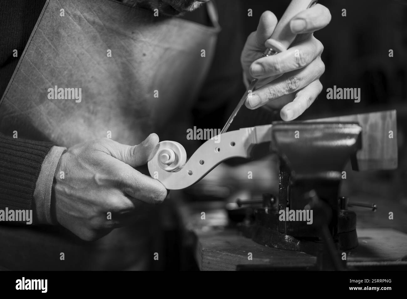 Artigiano che scolpisce un dettaglio a spirale in legno su un rotolo di violino con uno scalpello Foto Stock