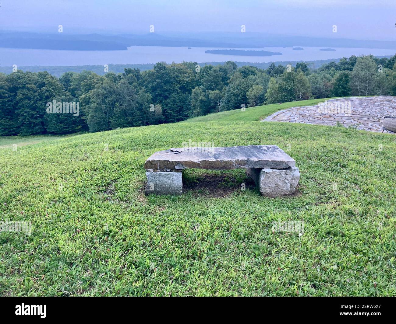 Abbracciando la serenità della natura, una panchina solitaria arroccata su una montagna offre il luogo perfetto per ammirare la vista mozzafiato di un tranquillo lago b - Immagine stock catturata con smartphone