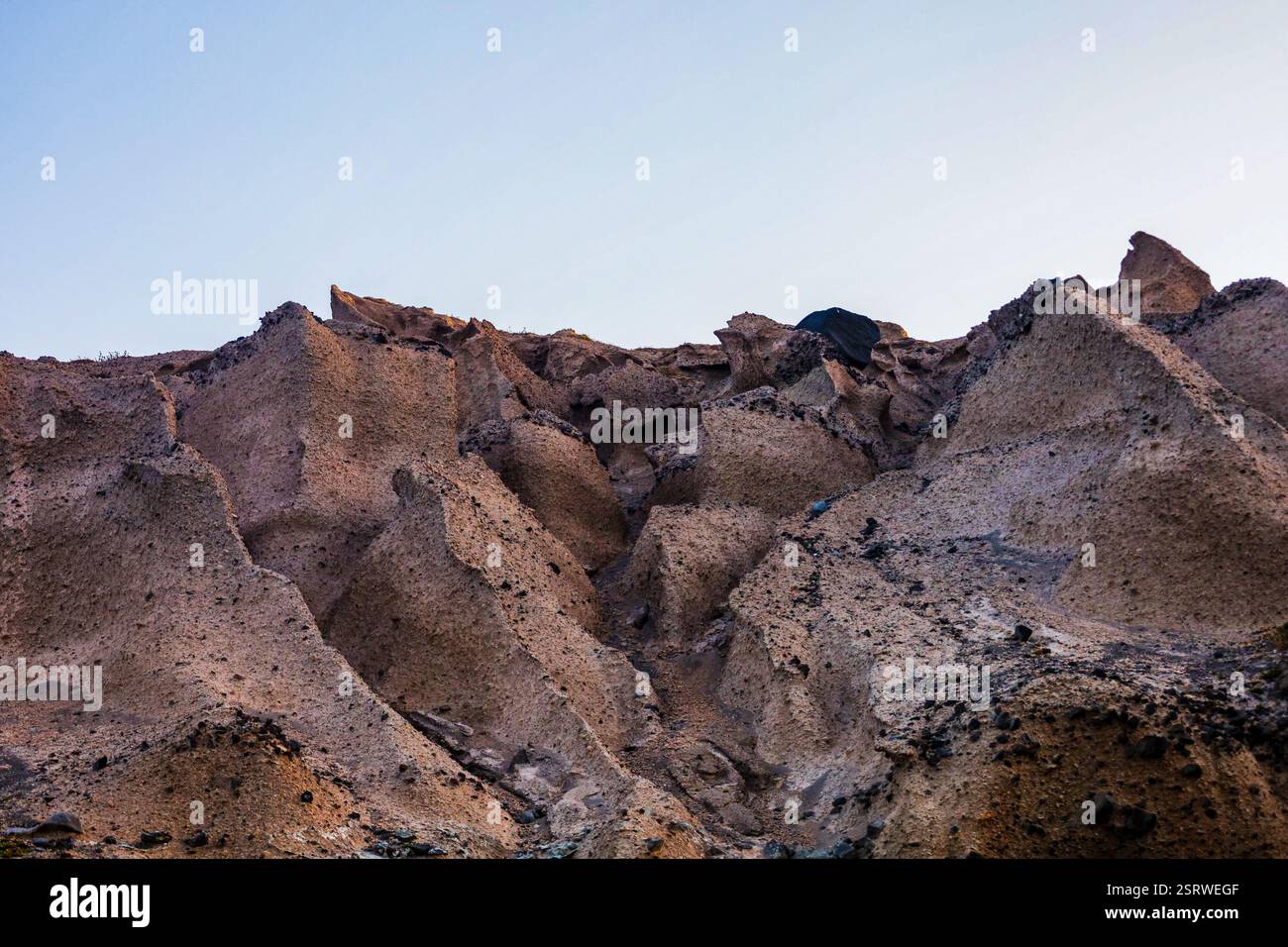 Una vista suggestiva delle aspre formazioni rocciose vulcaniche scolpite dall'erosione, che si stagliano contro un cielo blu morbido Foto Stock