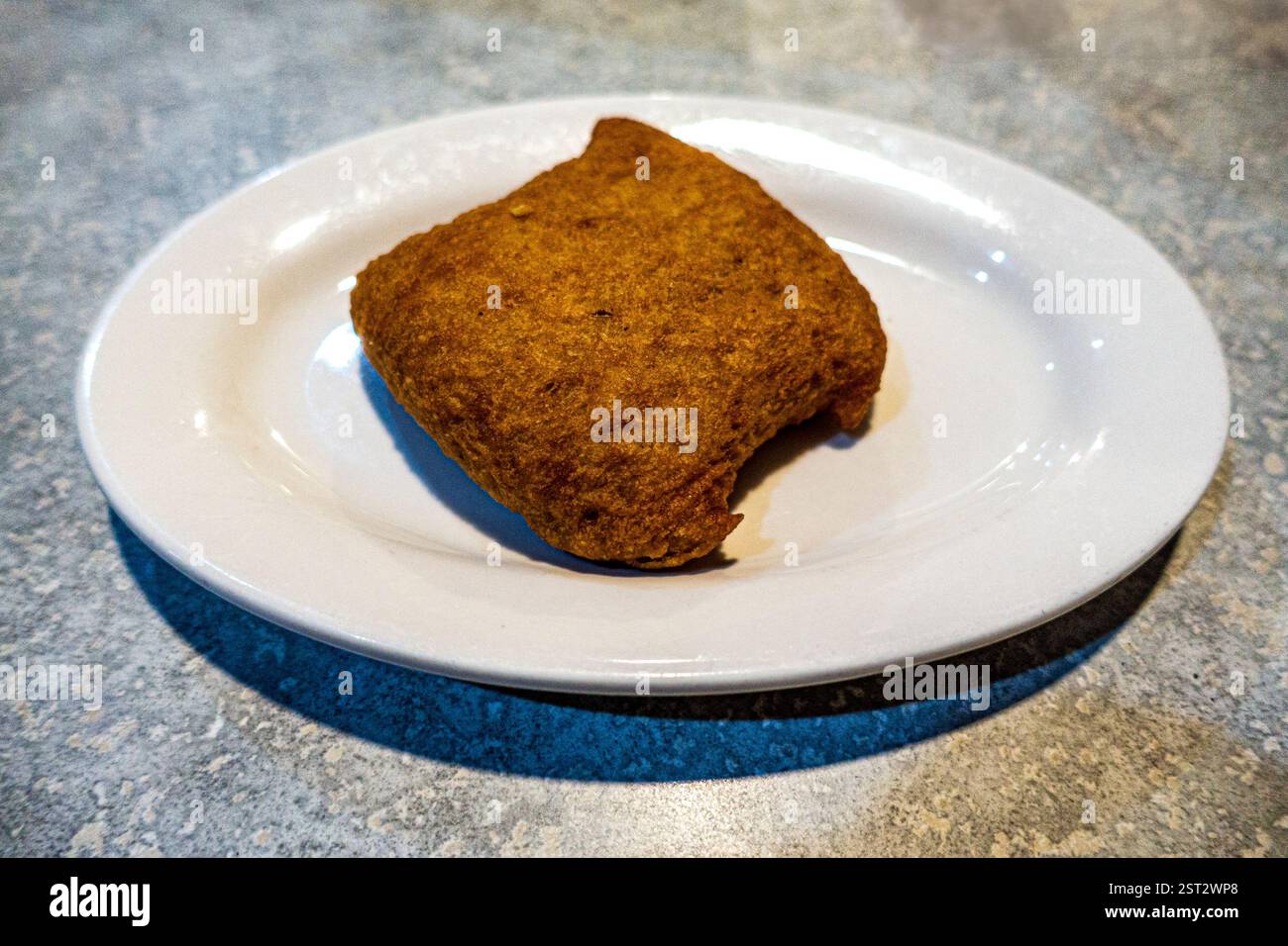 Una crosta quadrata dorata con crosta croccante e friabile si trova su un semplice piatto bianco. Il suo esterno caldo ricorda il saporito ripieno all'interno. La piastra si appoggia a. Foto Stock
