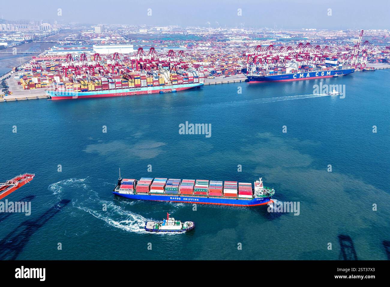 QINGDAO, CINA - 17 FEBBRAIO 2025 - Una nave cargo carica di container per il commercio estero lascia il porto di Qingdao con l'assistenza di un rimorchiatore Foto Stock