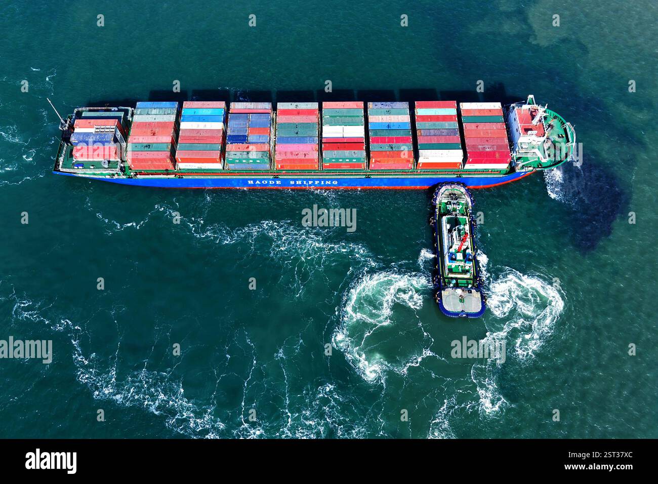 QINGDAO, CINA - 17 FEBBRAIO 2025 - Una nave cargo carica di container per il commercio estero lascia il porto di Qingdao con l'assistenza di un rimorchiatore Foto Stock