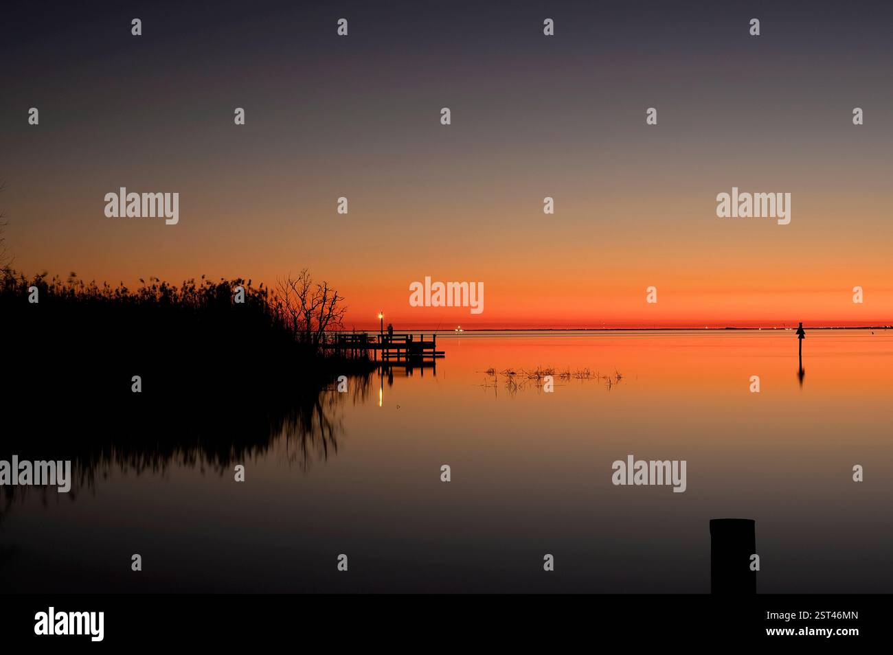 Tramonto tranquillo su un lago calmo con riflessi e un molo in legno Foto Stock