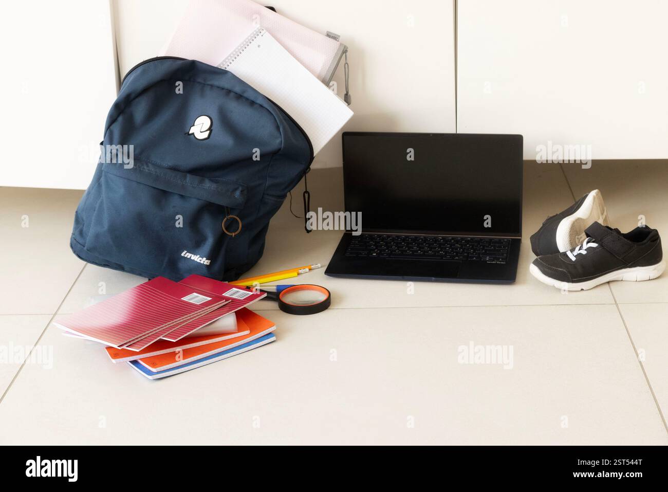 Zaino scolastico, laptop, sneaker e oggetti sparsi per terra, che mostrano il disordine quotidiano Foto Stock
