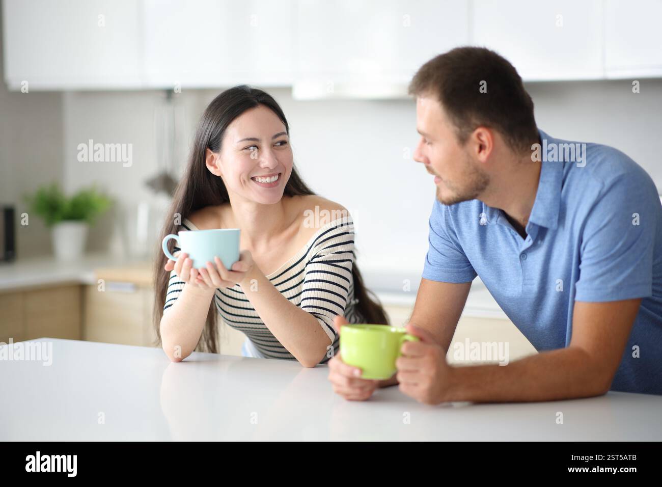 Coppia interrazziale che parla e beve in cucina a casa Foto Stock