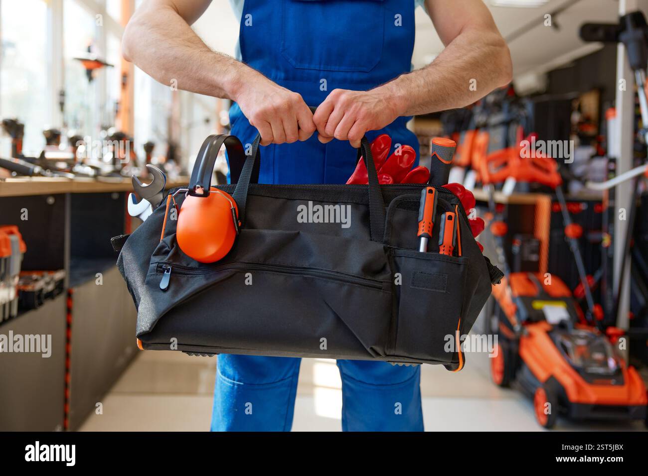 Colpo ritagliato di un riparatore o di un operaio edile che trasporta una borsa portautensili Foto Stock