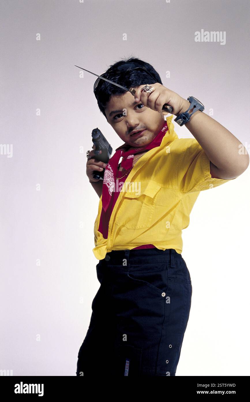 Bambino vestito e comportato come un tipico criminale, ragazzo che indossa abiti sgargianti e tiene in mano il coltello Rampuri e la pistola modello numero di rilascio 498 Foto Stock