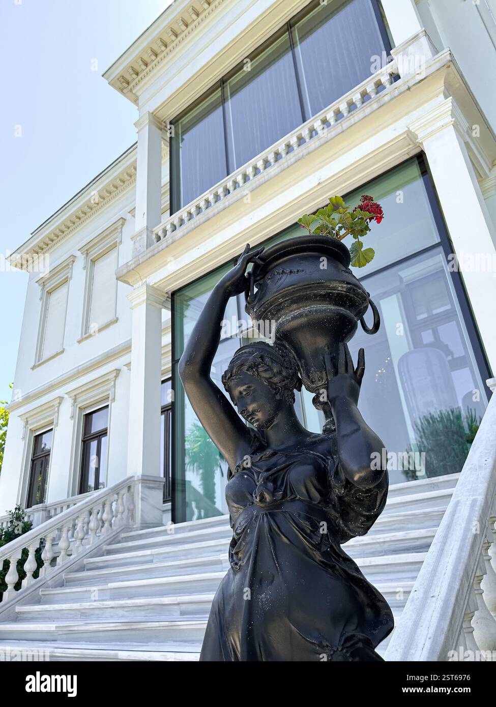 Questa elegante fotografia cattura un primo piano di una statua nera di una donna che regge con grazia un vaso decorativo con fiori rossi, appoggiato sul dorso Foto Stock