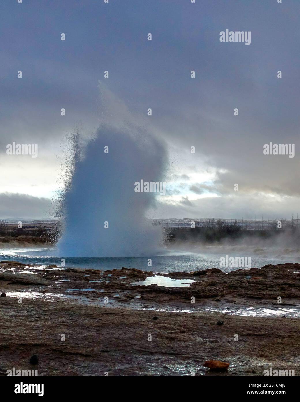 Potente eruzione del geyser islandese, sparando una colonna di acqua bollente e vaporizzando in aria contro un cielo spettacolare e una roccia vulcanica. Foto Stock