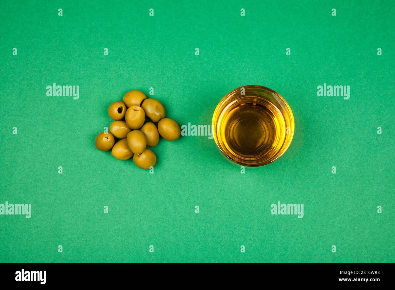 rigenera olive e un bicchiere di olio d'oliva su sfondo verde. La semplice composizione evidenzia l'origine naturale, il gusto puro e il sano Mediterraneo Foto Stock