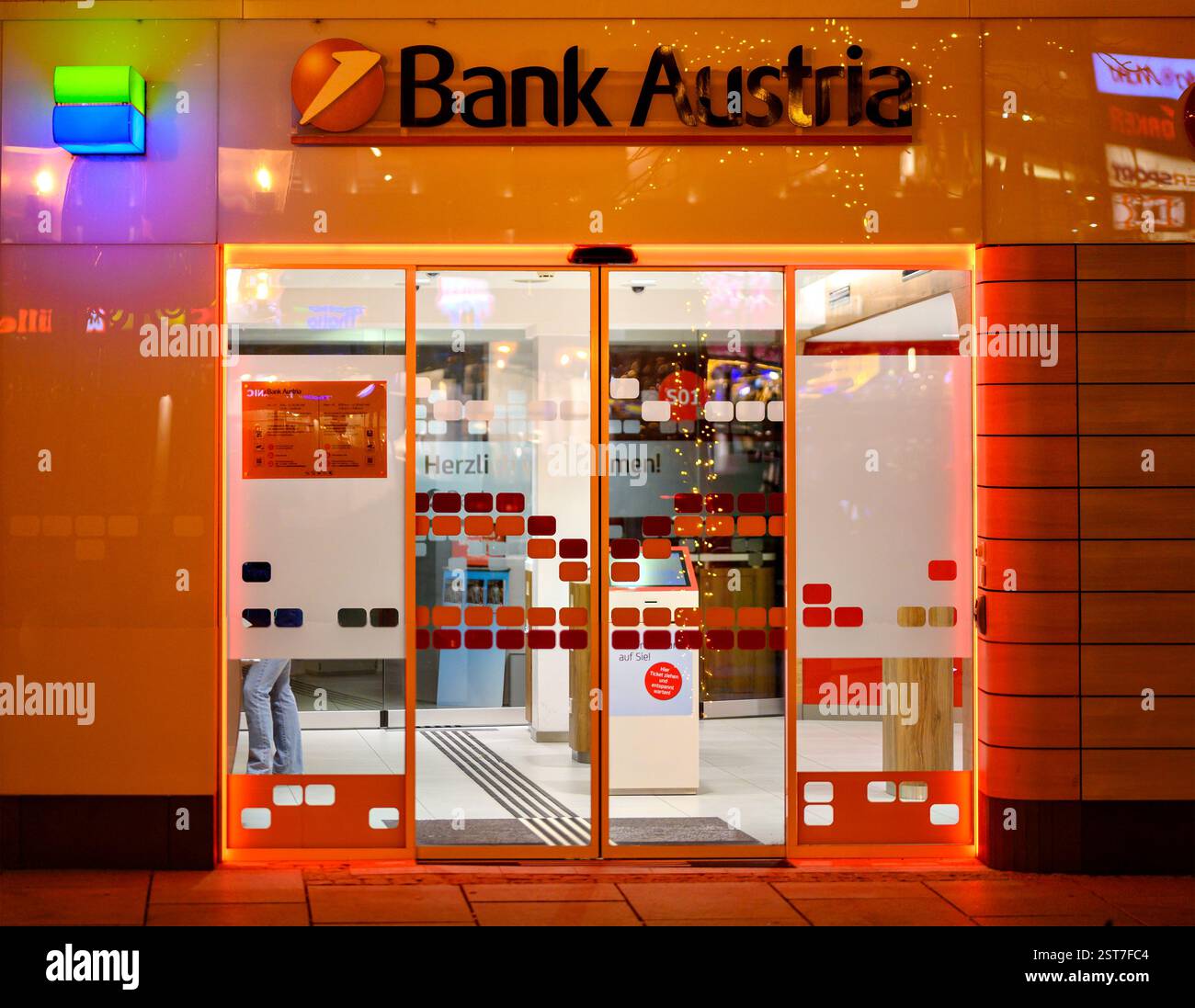 Ingresso illuminato di colore arancione a una filiale della Bank Austria di notte nella città di Tulln in Austria Foto Stock