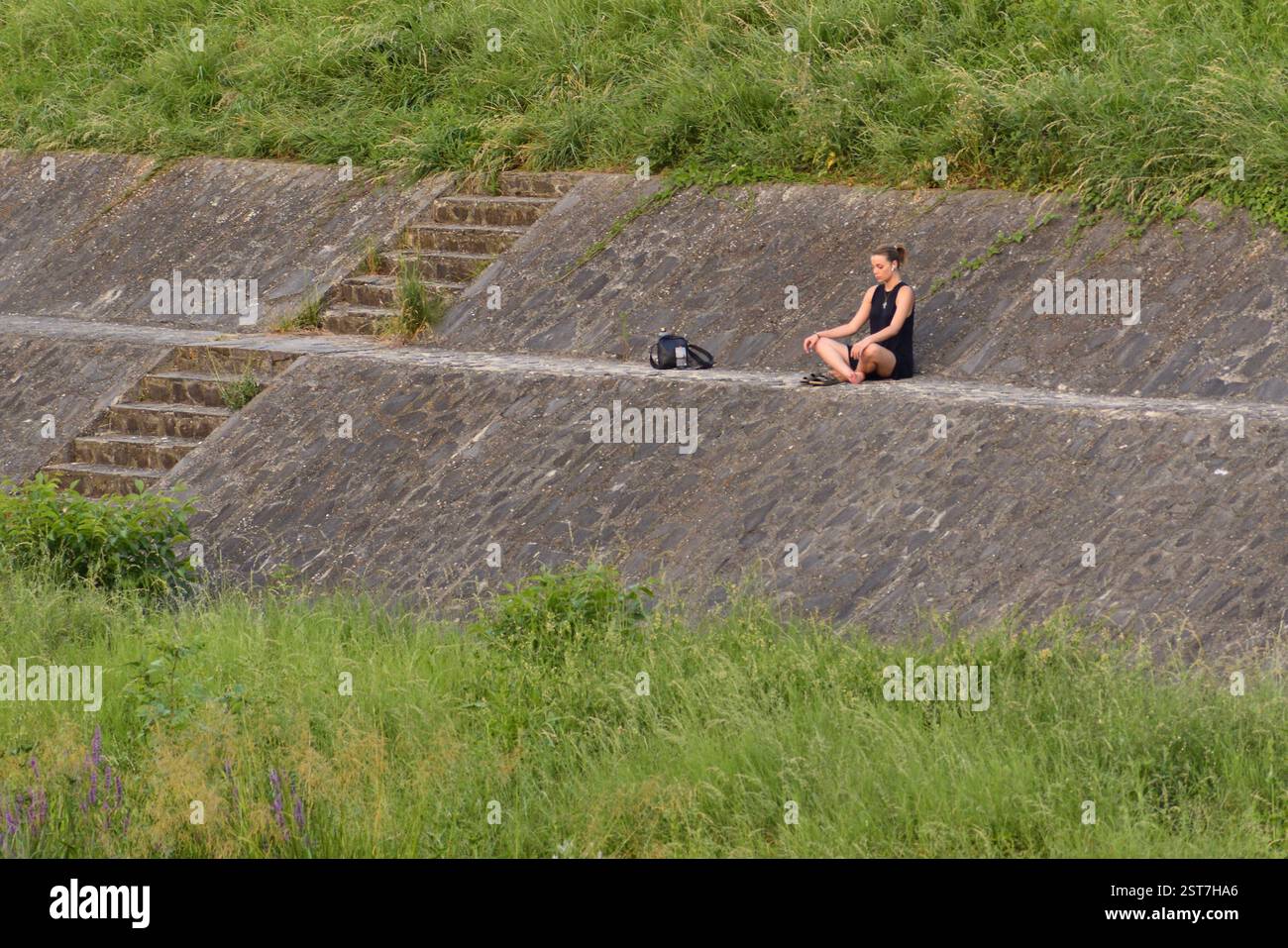 Giovane donna che fa yoga sulle rive del fiume in un pomeriggio estivo Foto Stock