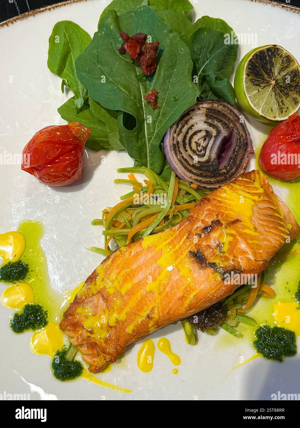 Questo piatto splendidamente placcato presenta un filetto di salmone perfettamente scottato con una crosta dorata, condita con una vivace salsa gialla. Si appoggia su un letto di Foto Stock