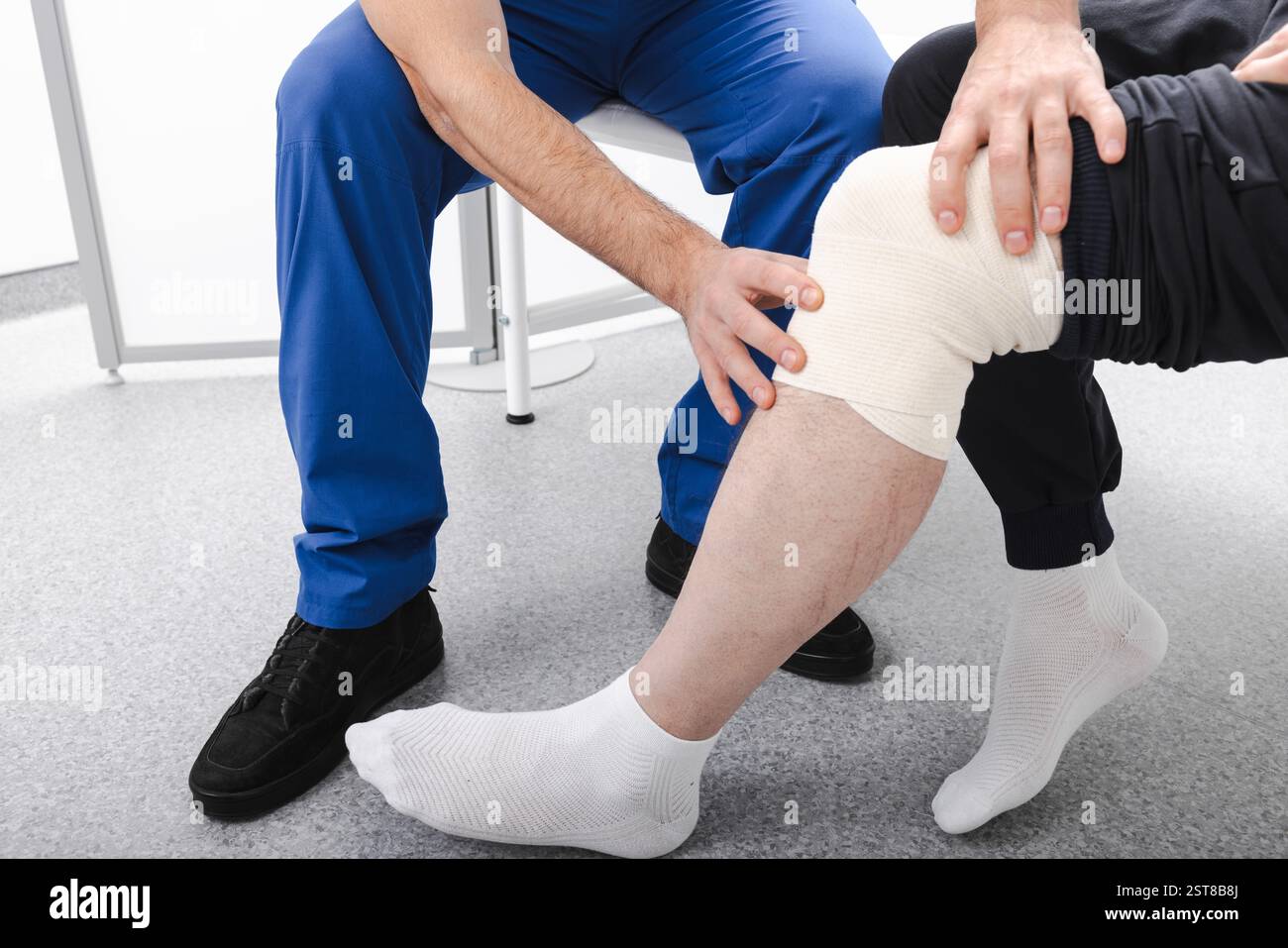 Il fisioterapista bende il ginocchio di un paziente con una fascia elastica per fissare il ginocchio in una posizione fissa. Lesioni al ginocchio e trattamento Foto Stock