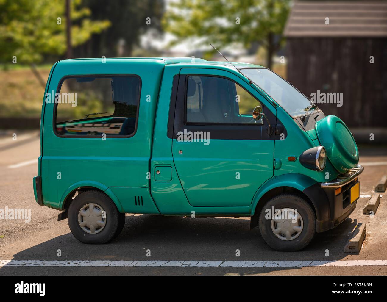 Una microcar giapponese turchese compatta con un design unico arrotondato, parcheggiata in una soleggiata, che mostra le sue dimensioni ridotte e l'aspetto eccentrico con cui è stata catturata Foto Stock