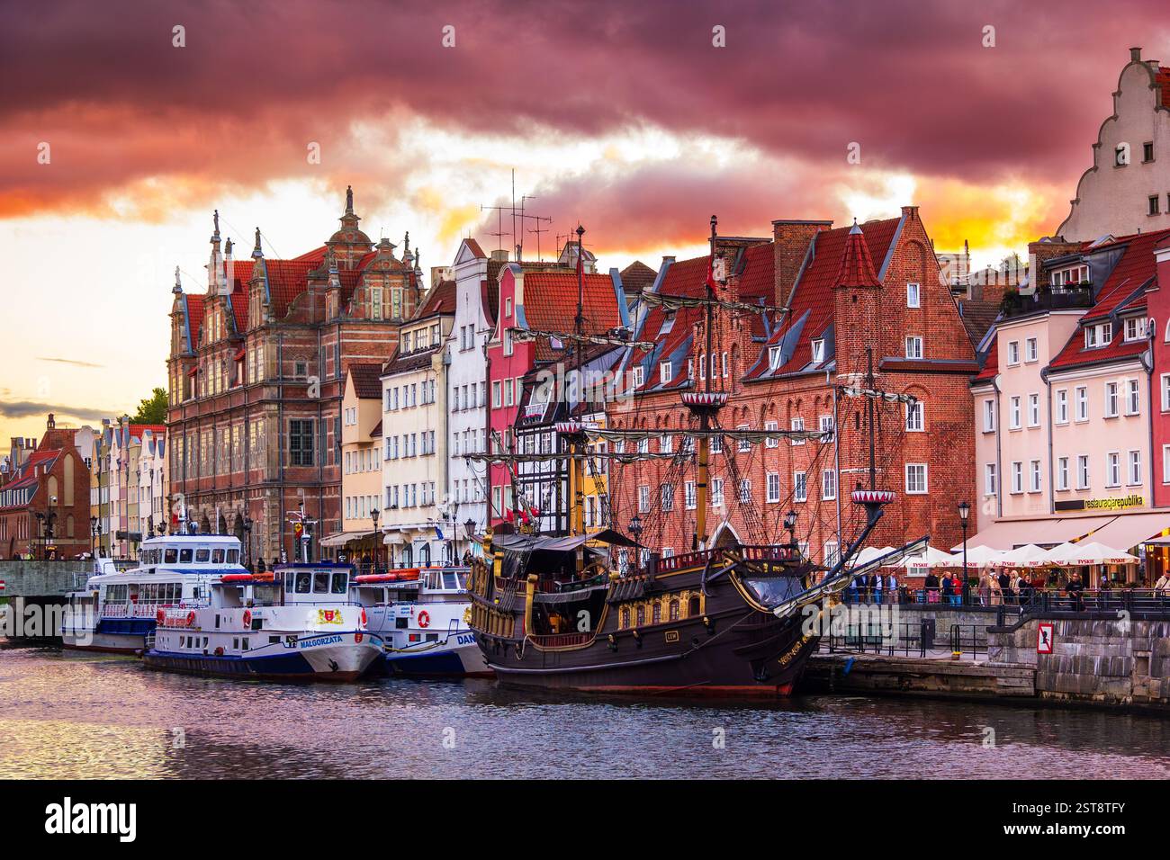 Splendida e colorata vista serale del centro di Danzica, nella Polonia settentrionale. Tramonto sul fiume Motlawa. Vista di barche, navi, alte case e cielo colorato. Foto Stock