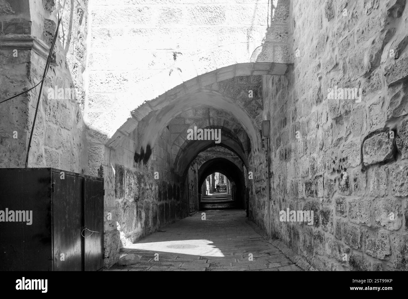 Uno stretto tunnel buio con una porta nera alla fine Il tunnel è vuoto e la luce splende sul muro Foto Stock