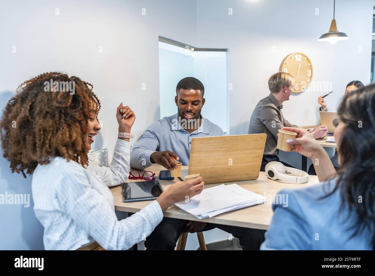 Team diversificati che lavorano insieme in uno spazio di coworking, utilizzando laptop e bevendo caffè, godendo di un ambiente di lavoro produttivo e collaborativo Foto Stock